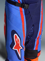 Alpinestars 2026 Techstar Nomur Pants, Motocross Pants in Dark Navy Orange and UCLA Blue, close-up showing the SX2 magnetic buckle waist closure, laser-cut perforations on the thigh, and iconic star logo, durable off-road racing gear.