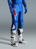 Alpinestars 2026 Fluid Grid Hose, Motocross-Hose, Blau und Rot, getragen mit weißen Motocross-Stiefeln und blauen Handschuhen, mit einem großen roten Stern-Logo auf dem Oberschenkel und schwarzen Knie-Innenpaneelen, konzipiert für den Offroad-Einsatz.