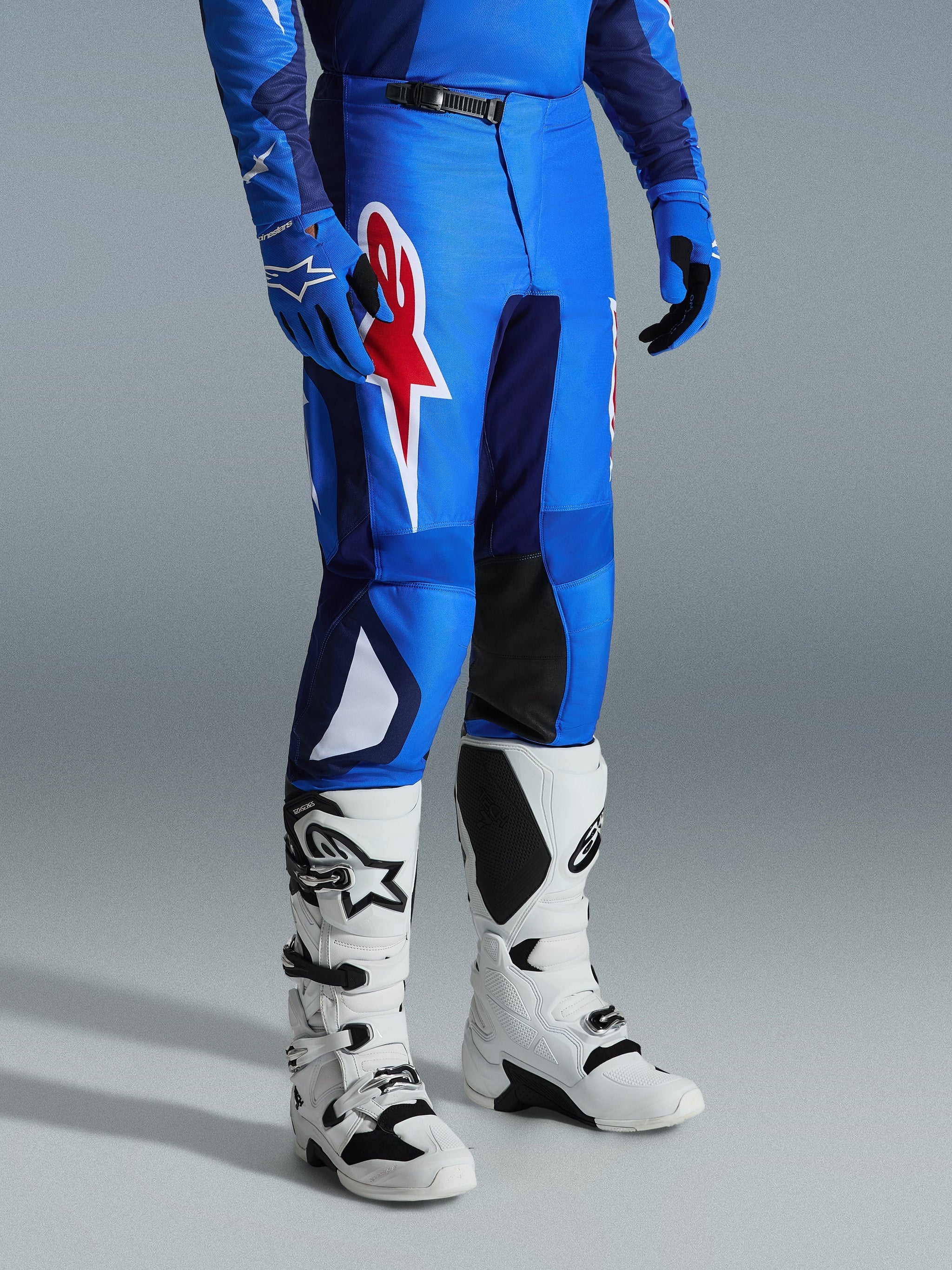 Alpinestars 2026 Fluid Grid Hose, Motocross-Hose, Blau und Rot, getragen mit weißen Motocross-Stiefeln und blauen Handschuhen, mit einem großen roten Stern-Logo auf dem Oberschenkel und schwarzen Knie-Innenpaneelen, konzipiert für den Offroad-Einsatz.