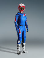 Motocross-Fahrer in kompletter Rennausrüstung, blau-rotes Trikot mit Gittermuster und Alpinestars-Logo, 2026 Fluid Grid Hose in Blau-Rot mit schwarzen Knieinnenseiten, rot-weißer Helm mit Schutzbrille, weiß-schwarze Stiefel, blaue Handschuhe, abgestimmtes Outfit für Offroad-Rennsport