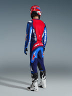 Motocross-Fahrer in der Rückansicht mit Alpinestars 2026 Fluid Grid Hose in Blau-Rot, passendes blau-rotes Trikot mit weißen Logos, rot-weißer Helm, weiß-schwarze Stiefel, koordinierte Ausrüstung für Offroad-Rennen
