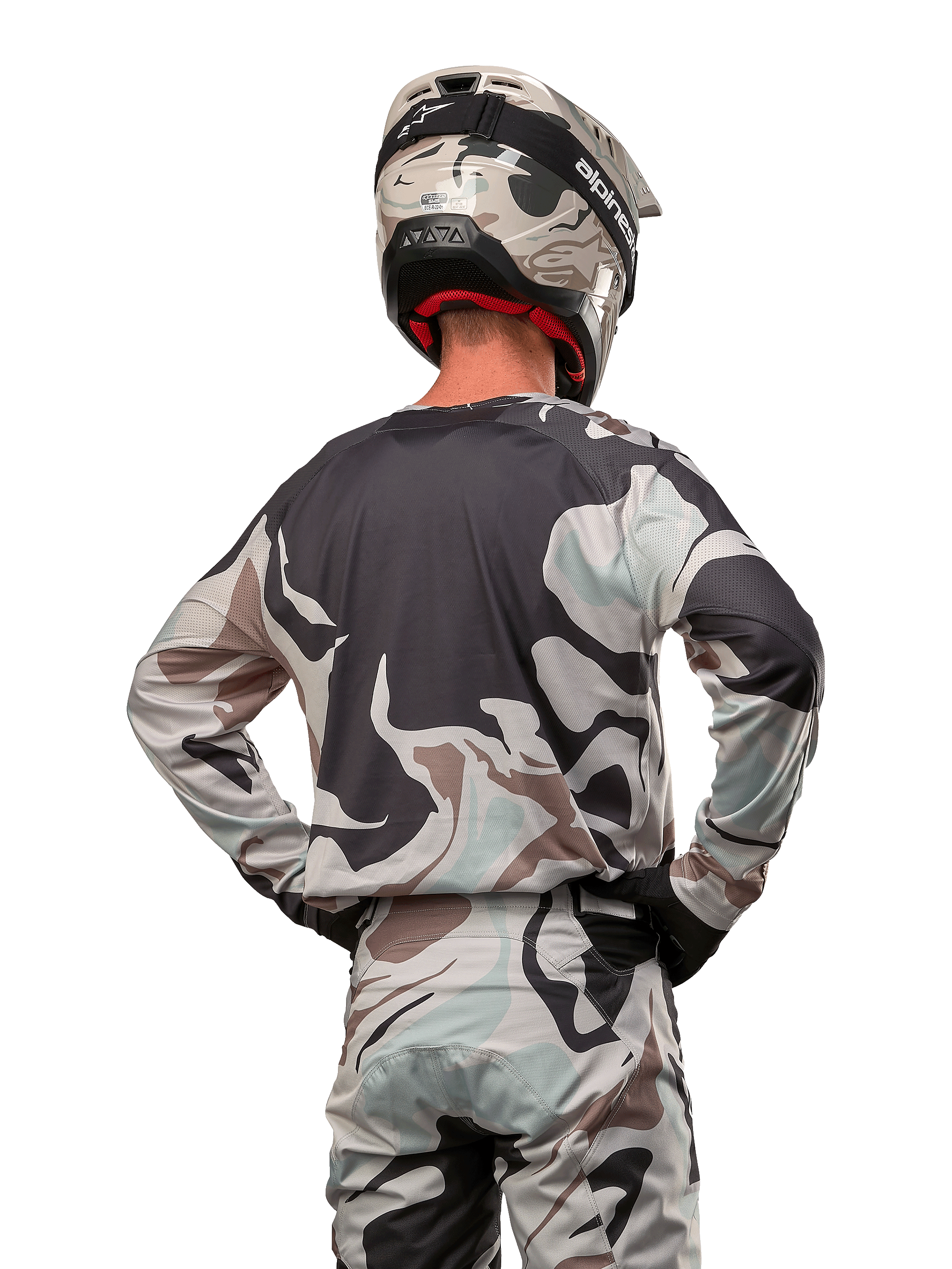 Motocross-Fahrer in der Rückansicht, Alpinestars 2024 Racer Tactical Jersey in Iron Camo Dust Gray, passende Camouflage-Hose und Helm, Hände an den Hüften, abgestimmte Offroad-Rennausrüstung