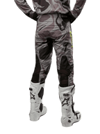 Alpinestars 2024 Racer Tactical Hose, Motocross-Hose, Cast Gray Camo Magnet, Rückansicht zeigt Camouflage-Muster und schwarze atmungsaktive Stretch-Zonen, getragen mit weiß-schwarzen Motocross-Stiefeln, entwickelt für Offroad-Rennsport.
