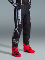 Alpinestars 2026 Fluid Apex Pants, Motocross Pants, Black and Gray, worn with vibrant pink and red boots and matching black and white jersey, featuring bold vertical Alpinestars branding on the thigh, reinforced panels, and ratchet waist closure for off-road performance.