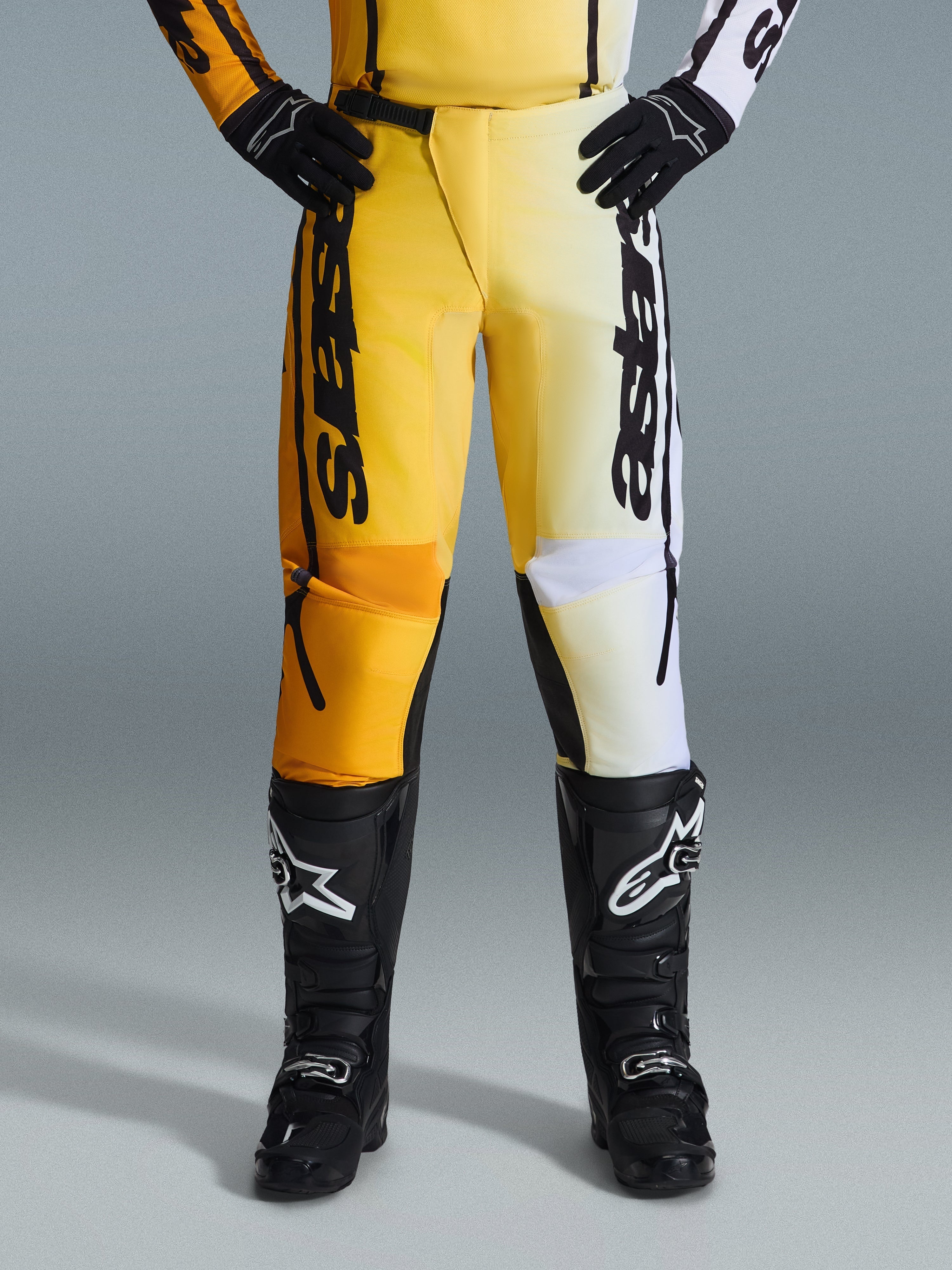 Alpinestars 2026 Fluid Apex Hose, Motocross-Hose, Gelb und Schwarz, Split-Color-Design mit gelben und weißen Einsätzen, markantes vertikales „astars“-Branding, getragen mit schwarzen Motocross-Stiefeln und Handschuhen, Performance-Ausrüstung für den Offroad-Sport