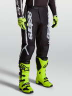 Alpinestars Fluid Apex V2 Hose, Motocross-Ausrüstung für Herren, Schwarz und Silber, mit 600D-Polygewebe, getragen mit neongelben Stiefeln.