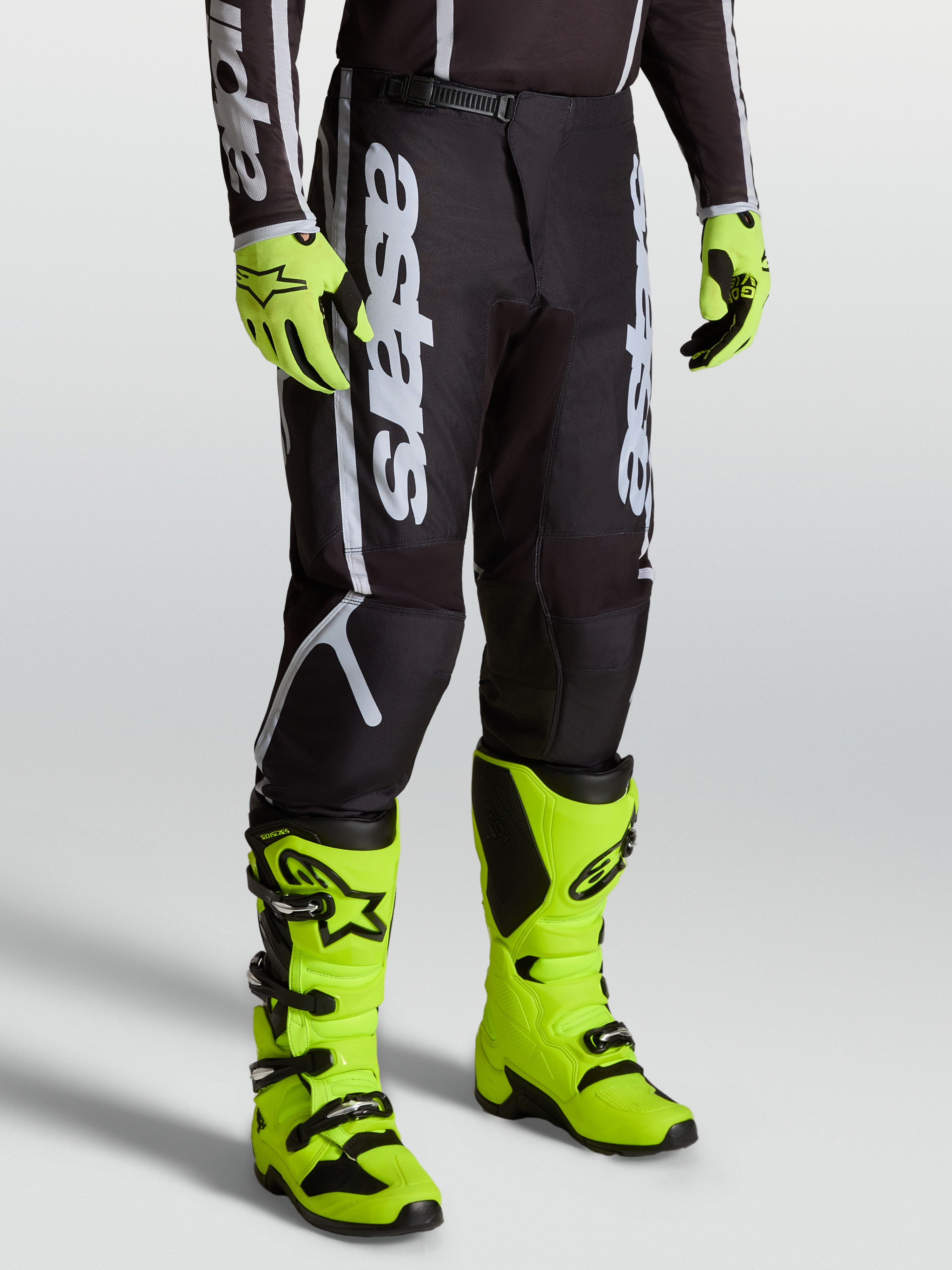 Alpinestars Fluid Apex V2 Hose, Motocross-Ausrüstung für Herren, Schwarz und Silber, mit 600D-Polygewebe, getragen mit neongelben Stiefeln.