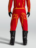 Alpinestars Fluid Apex V2 Hose, Motocrosshose für Herren in Feuerrot und Gold, Rückansicht mit schwarzen Motorradstiefeln.