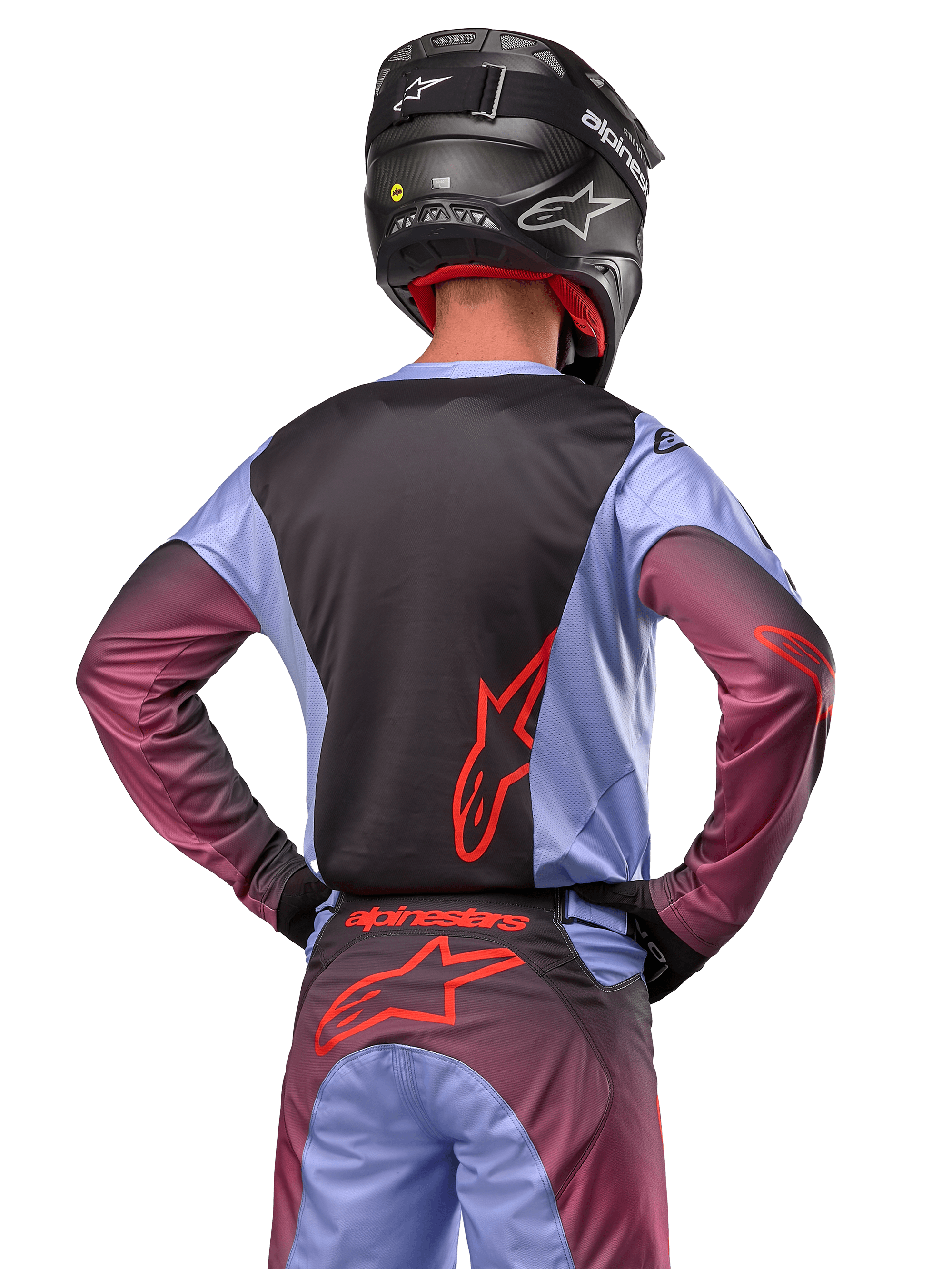Motocross-Fahrer von hinten, trägt Alpinestars 2024 Racer Hoen Ausrüstung, Trikot in Lavan Purple und Schwarz mit rotem Logo, passende Hose mit roten Akzenten, schwarzer Helm, abgestimmtes Outfit für Offroad-Rennen