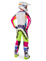 Motocross-Fahrer von hinten in Alpinestars Limited Edition Supertech Hay Ausrüstung, leuchtende mehrfarbige Supertech Hay Hose mit neongelben, pinken und lila Grafiken, passendes Trikot, weißer Helm und abgestimmte weiß-blaue Stiefel, komplettes Offroad-Rennoutfit