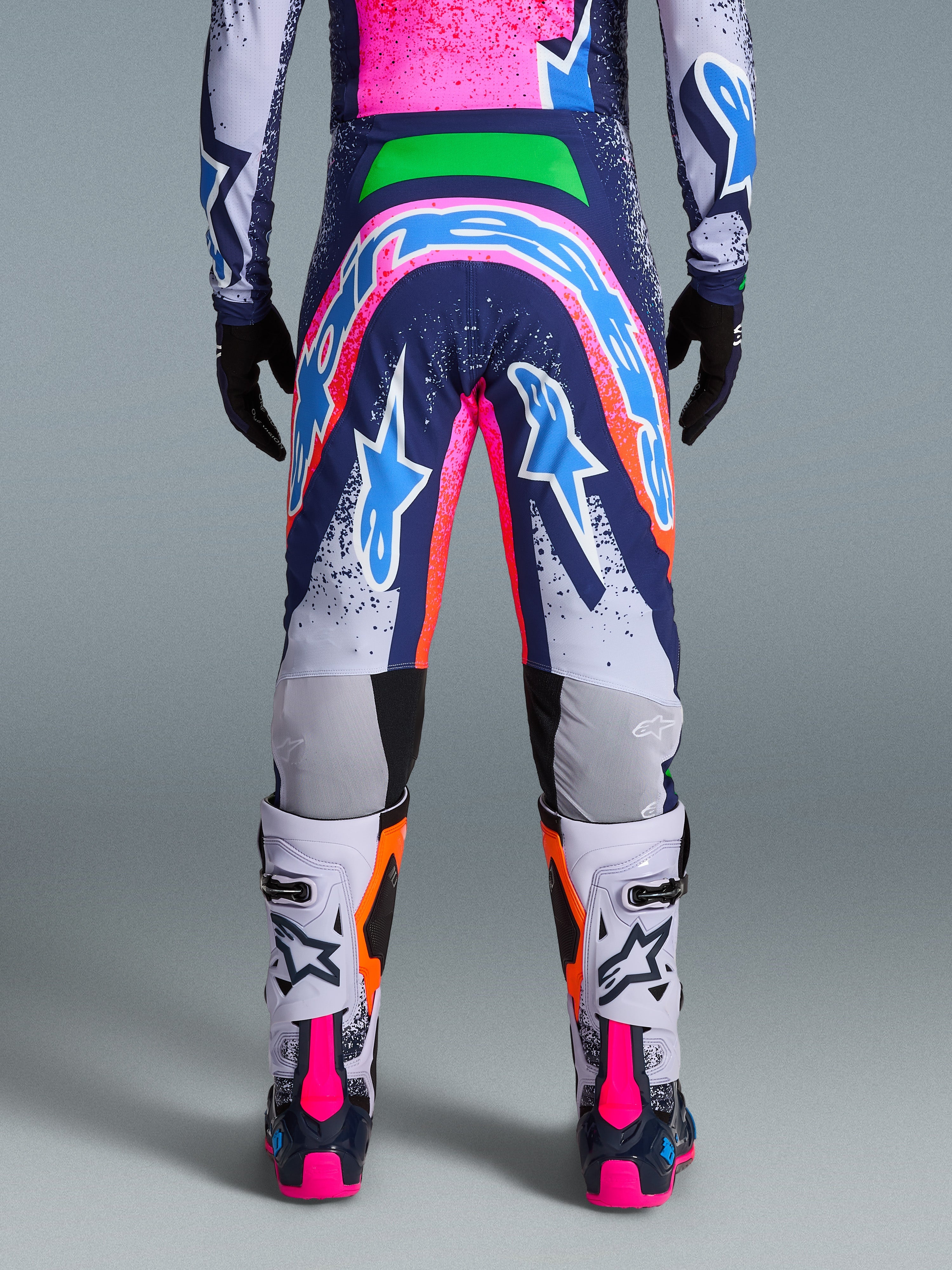 Alpinestars Limited Edition Supertech Records Hose, Motocross-Hose, Mehrfarbig mit leuchtenden pinken, blauen, orangefarbenen und weißen Grafiken, Rückansicht mit großem Logo auf dem Gesäß, getragen mit passendem Jersey und weißen Stiefeln, athletische Passform auf Profi-Niveau für den Offroad-Rennsport