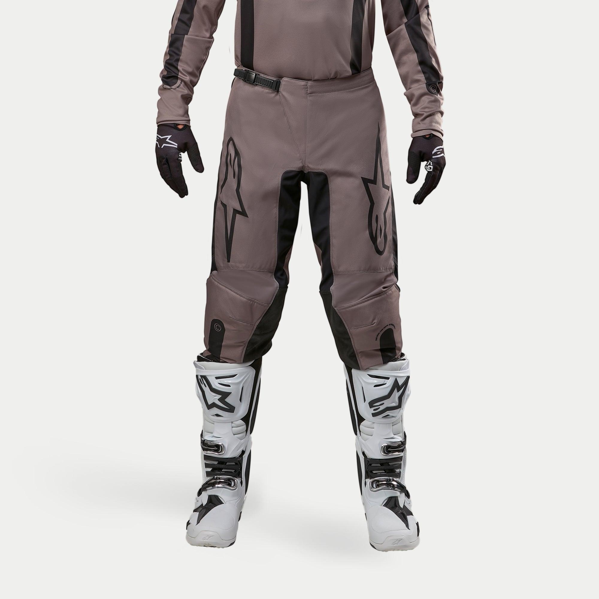 Alpinestars 2024 Fluid Lurv Hose, Motocross-Hose, Mud Black, getragen mit passendem Jersey, schwarzen Handschuhen und weißen Stiefeln, mit großen schwarzen Logos auf den Oberschenkeln, ergonomischer Passform und strapazierfähigem Material für Offroad-Rennen