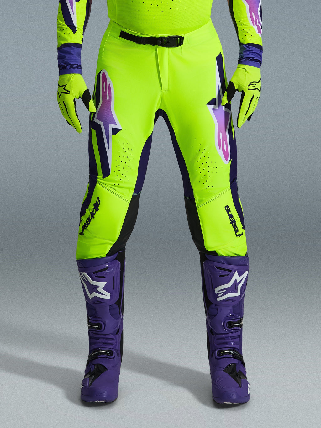 Alpinestars 2026 Supertech Vista Hose, Motocross-Hose, Neongelb, Lila und Schwarz, kombiniert mit passenden Handschuhen und lila Stiefeln, mit großen Logos mit Farbverlauf auf den Oberschenkeln, perforierten Zonen zur Belüftung und einem professionellen athletischen Design für den Offroad-Rennsport