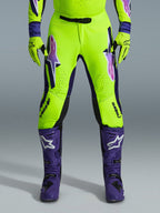 Alpinestars 2026 Supertech Vista Hose, Motocross-Hose, Neongelb, Lila und Schwarz, kombiniert mit passenden Handschuhen und lila Stiefeln, mit großen Logos mit Farbverlauf auf den Oberschenkeln, perforierten Zonen zur Belüftung und einem professionellen athletischen Design für den Offroad-Rennsport
