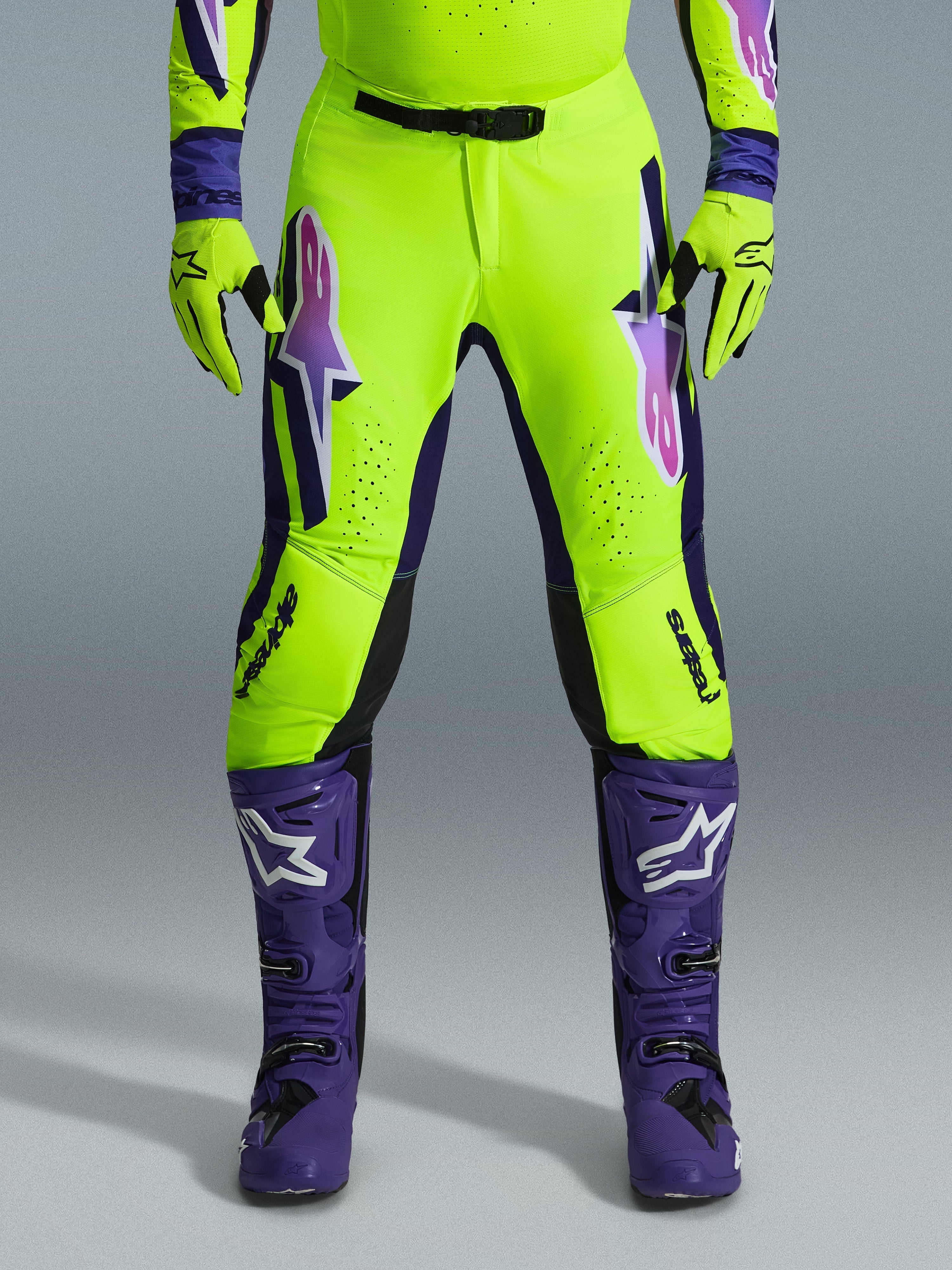 Alpinestars 2026 Supertech Vista Hose, Motocross-Hose, Neongelb, Lila und Schwarz, kombiniert mit passenden Handschuhen und lila Stiefeln, mit großen Logos mit Farbverlauf auf den Oberschenkeln, perforierten Zonen zur Belüftung und einem professionellen athletischen Design für den Offroad-Rennsport