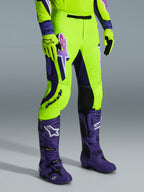 Alpinestars 2026 Supertech Vista Hose, Motocross-Hose, Leuchtendes Neongelb, Lila und Schwarz, getragen mit passenden lila Stiefeln und gelben Handschuhen, mit auffälligem Branding am Oberschenkel und einer athletischen Performance-Passform.