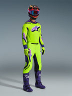 Alpinestars 2026 Supertech Vista Hose, Motocross-Hose, Neongelb und Lila, getragen mit passendem Renntrikot, lila Stiefeln und farbenfrohem Helm, mit schwarzen Leder-Kniepanels, markanten lila Astar-Logos und perforierten Belüftungszonen, koordiniertes Outfit für den Offroad-Rennsport.