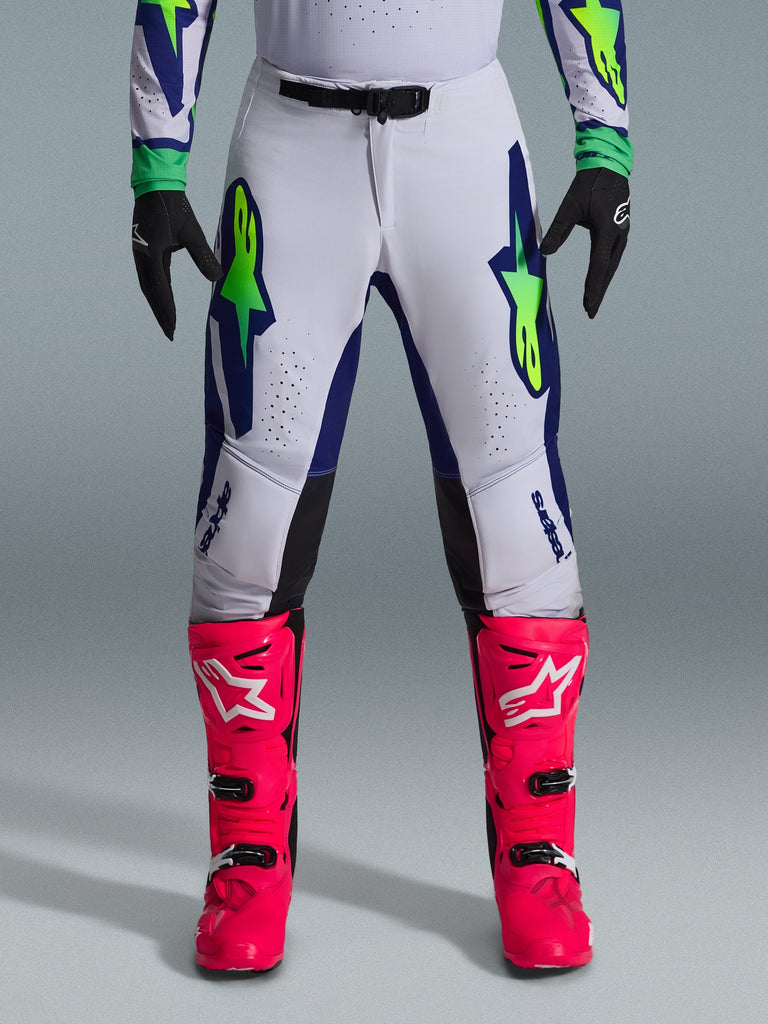 Alpinestars 2026 Supertech Vista Hose, Motocross-Hose, Hellgrau mit Akzenten in Gelb Fluo und Blau, kombiniert mit leuchtend pinken Stiefeln und schwarzen Handschuhen, auffällige Stern-Logos auf den Oberschenkeln und lasergeschnittene Perforationen für optimale Belüftung