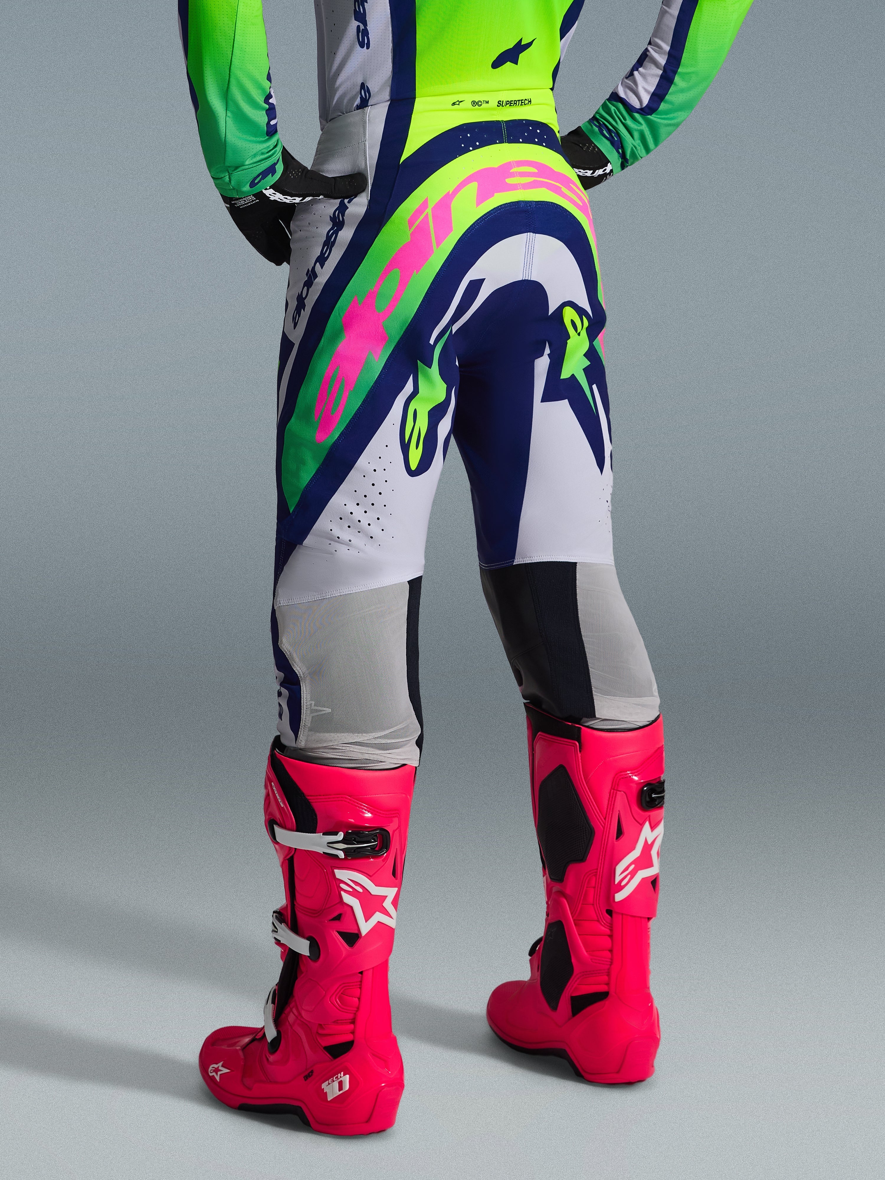 Alpinestars 2026 Supertech Vista Gear Set, rear view of motocross apparel, white pants with blue and lime green panels, large pink branding on seat, paired with vibrant pink Tech 10 boots, professional off-road racing gear