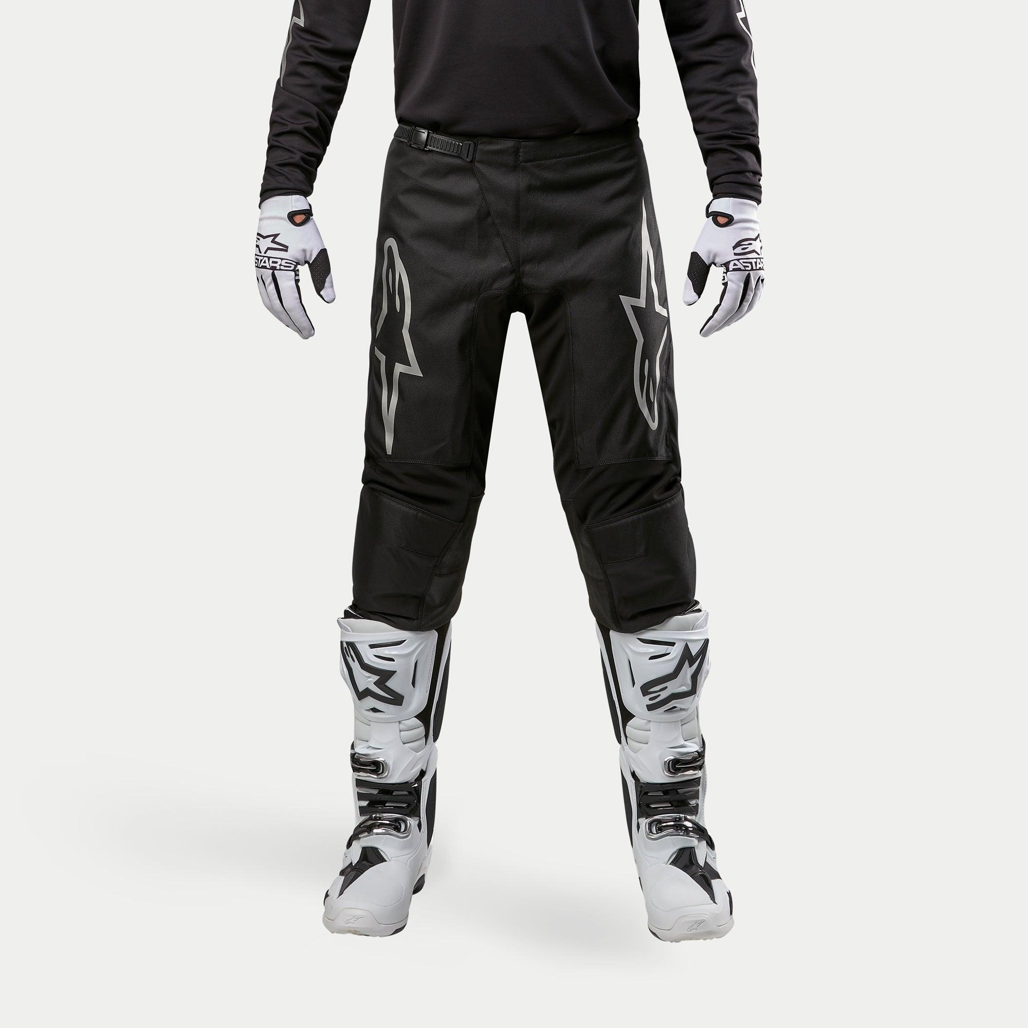 Alpinestars 2024 Fluid Graphite Pants, Motocross Pants, Black and Silver, featuring silver Alpinestars logos on the thighs, worn with white and black motocross boots and gloves, sporty design for off-road racing
