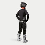 Alpinestars 2024 Fluid Graphite Pants, Motocross Pants, Black and Silver, rear view on a rider wearing a black jersey, black helmet, and white and black boots, featuring silver branding on the lower back and a durable poly-fabric construction for off-road racing