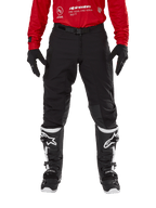 Alpinestars Techdura Hose, Enduro- und Offroad-Hose, Schwarz, getragen mit einem roten Alpinestars-Trikot und schwarz-weißen Stiefeln, mit robuster Stretch-Canvas-Konstruktion, verstellbarer magnetischer Gürtelschnalle und Knieverstärkungen aus Leder für Offroad-Performance.