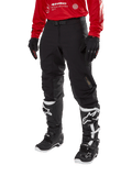Alpinestars Techdura Hose, schwarze Offroad-Motorradhose, kombiniert mit einem roten Langarm-Trikot und schwarz-weißen Motocross-Stiefeln, mit robuster Stretch-Polyamid-Konstruktion, Lederverstärkungen an den Knieinnenseiten und einem verstellbaren Gürtel mit Schnalle für den Enduro-Einsatz.