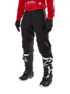 Alpinestars Techdura Hose, schwarze Offroad-Motorradhose, kombiniert mit einem roten Langarm-Trikot und schwarz-weißen Motocross-Stiefeln, mit robuster Stretch-Polyamid-Konstruktion, Lederverstärkungen an den Knieinnenseiten und einem verstellbaren Gürtel mit Schnalle für den Enduro-Einsatz.