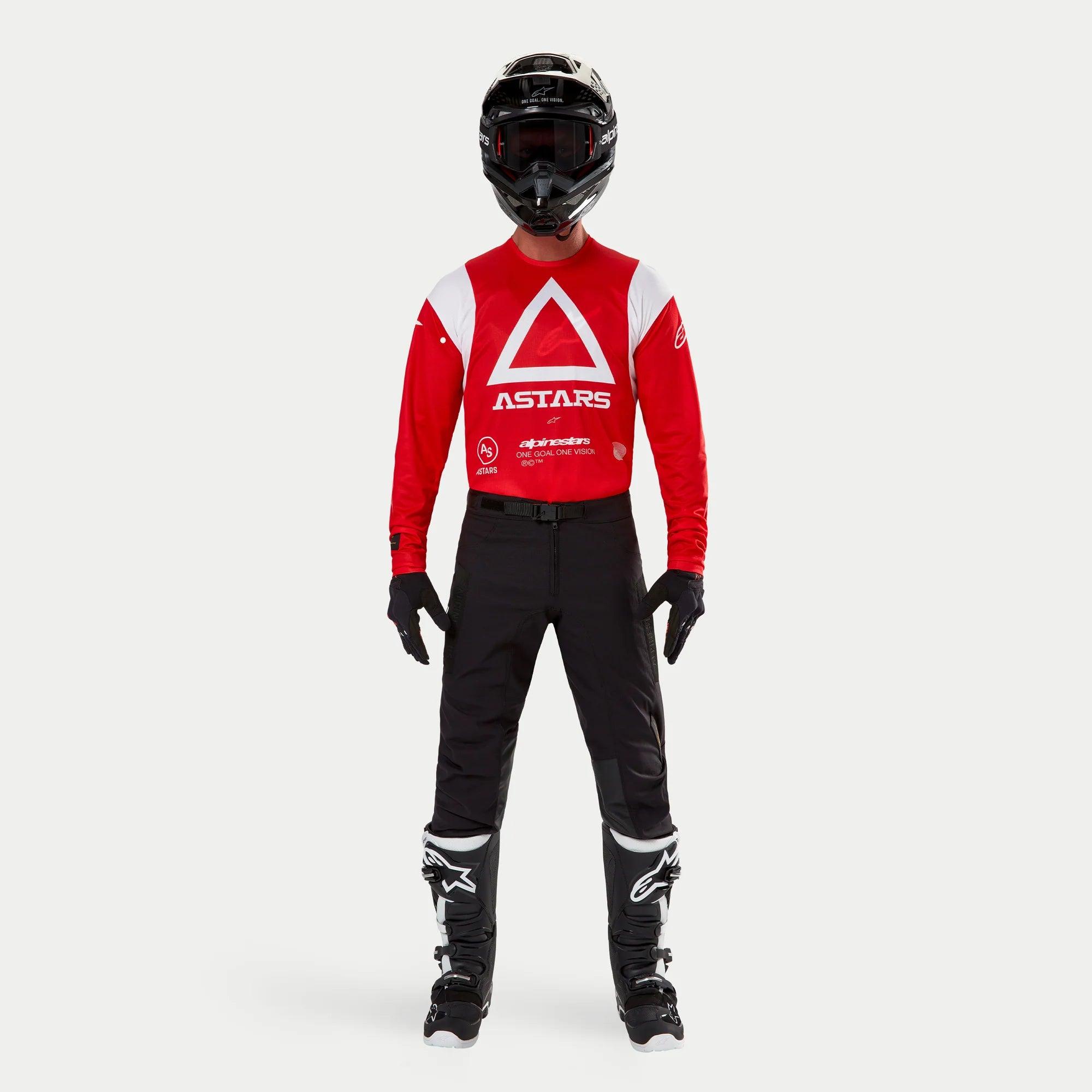 Alpinestars Techdura Hose, Enduro- und Offroad-Hose, Schwarz, kombiniert mit einem rot-weißen langärmeligen Astars-Trikot, schwarzem Helm und schwarz-weißen Stiefeln, mit robuster Stretch-Polyamid-Konstruktion und technischen Einsätzen für Offroad-Fahrten.