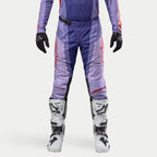 Alpinestars 2024 Techstar Ocuri Hose, Motocross-Hose in Lila und Hot Orange, strapazierfähiges Ripstop-Material, SX2 Magnetverschluss-Schnalle, Babel-Kniekonstruktion, kombiniert mit weißen Motocross-Stiefeln und schwarzen Handschuhen.
