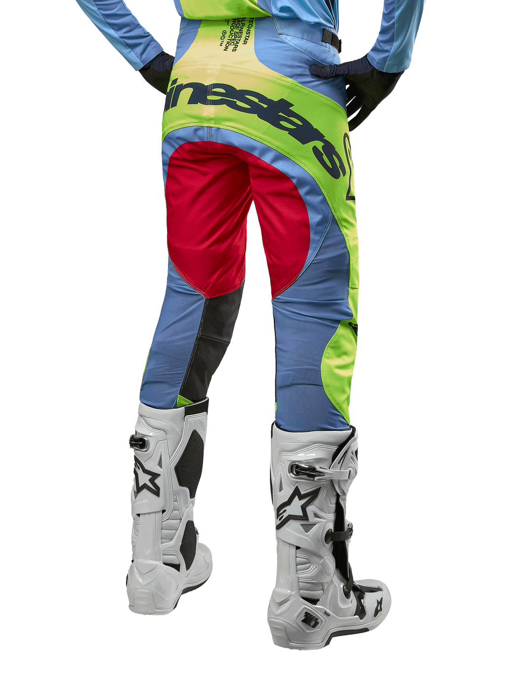 Alpinestars 2024 Techstar Ocuri Hose, Motocross-Hose, Hellblau, Gelb Fluo und Beerenrot, Rückansicht getragen mit weiß-schwarzen Motocross-Stiefeln, mit auffälligem Color-Blocking und markantem Alpinestars-Branding auf dem Gesäß.