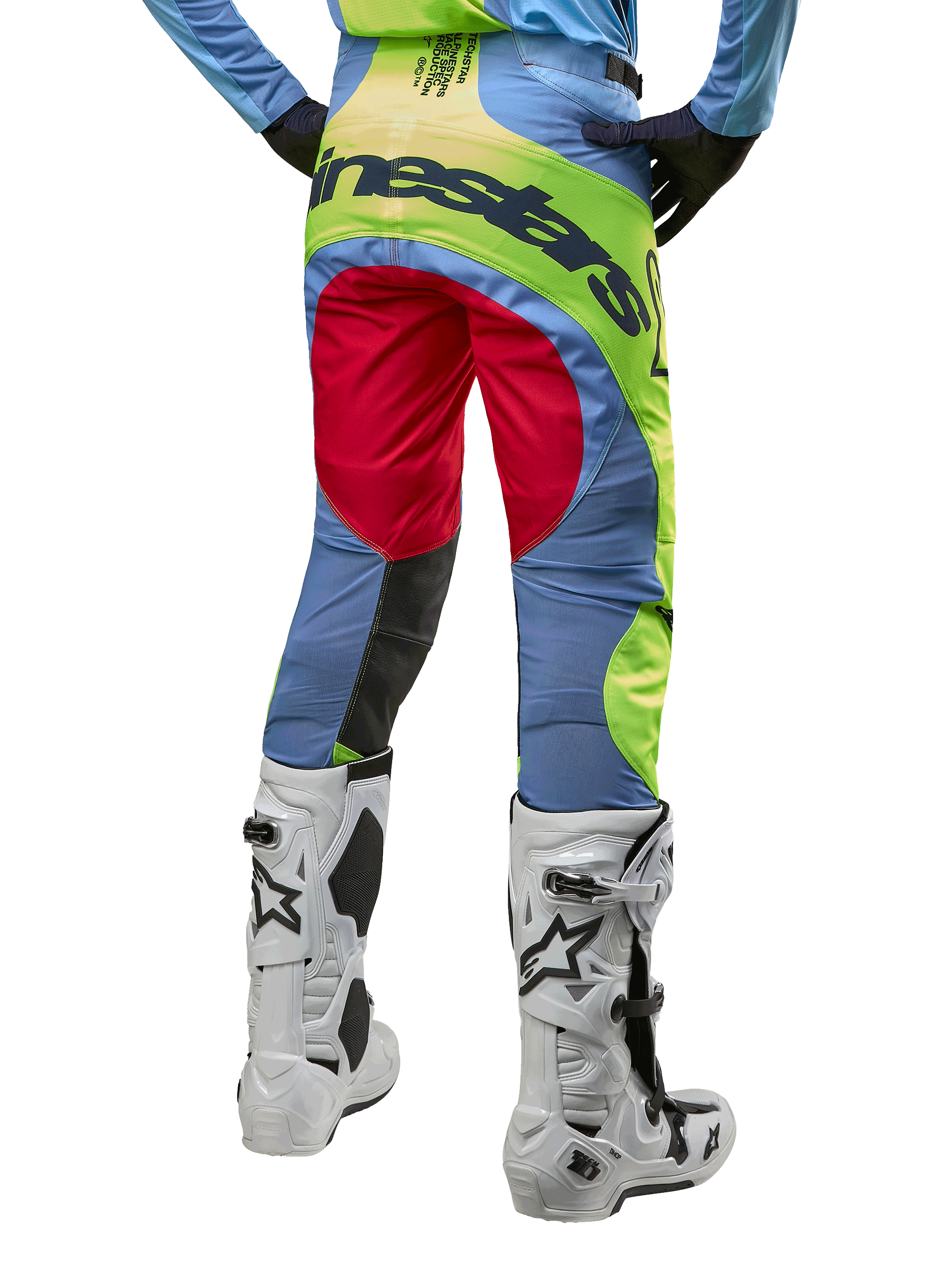 Alpinestars 2024 Techstar Ocuri Hose, Motocross-Hose, Hellblau, Gelb Fluo und Beerenrot, Rückansicht getragen mit weiß-schwarzen Motocross-Stiefeln, mit auffälligem Color-Blocking und markantem Alpinestars-Branding auf dem Gesäß.