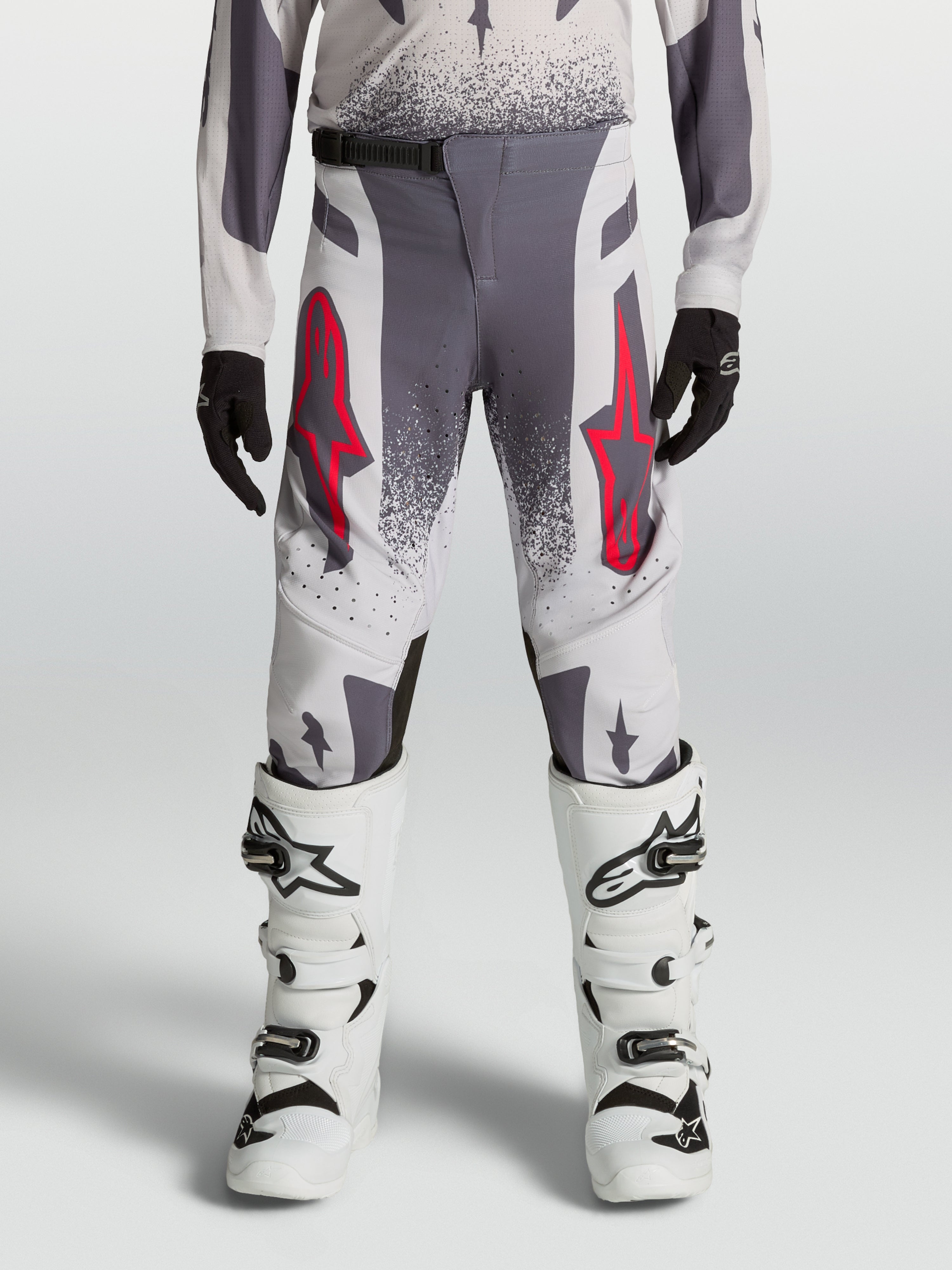 Alpinestars Jugend Supertech Swan Hose, Motocross-Rennhose in Grau und Lila mit roten Akzenten, getragen mit weißen Stiefeln.
