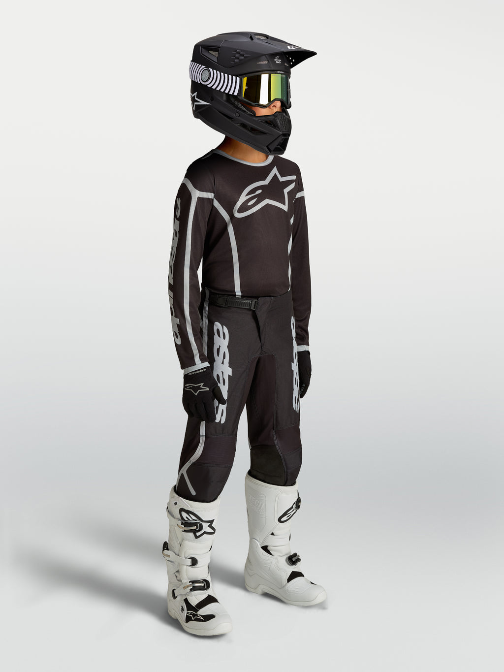 Alpinestars Jugend Fluid Apex V2 Hose, schwarz-silberne Motocross-Ausrüstung am Model mit Trikot, Helm und weißen Stiefeln.