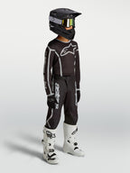Alpinestars Jugend Fluid Apex V2 Hose, schwarz-silberne Motocross-Ausrüstung am Model mit Trikot, Helm und weißen Stiefeln.