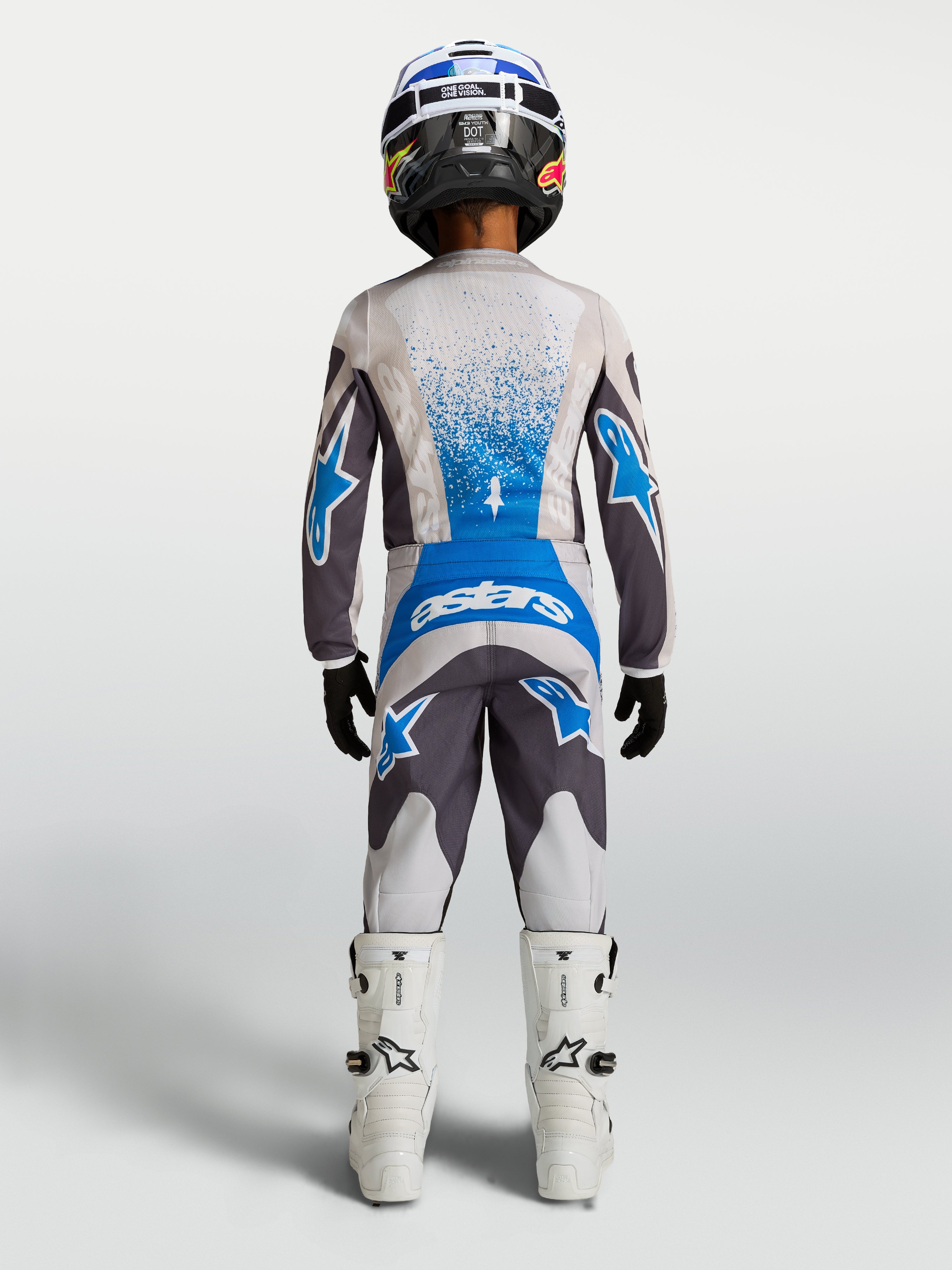 Alpinestars Fluid Drag Jugend-Hose 2027, Motocross-Hose für Kinder, Grau und Blau, Rückansicht mit Trikot und weißen Stiefeln.