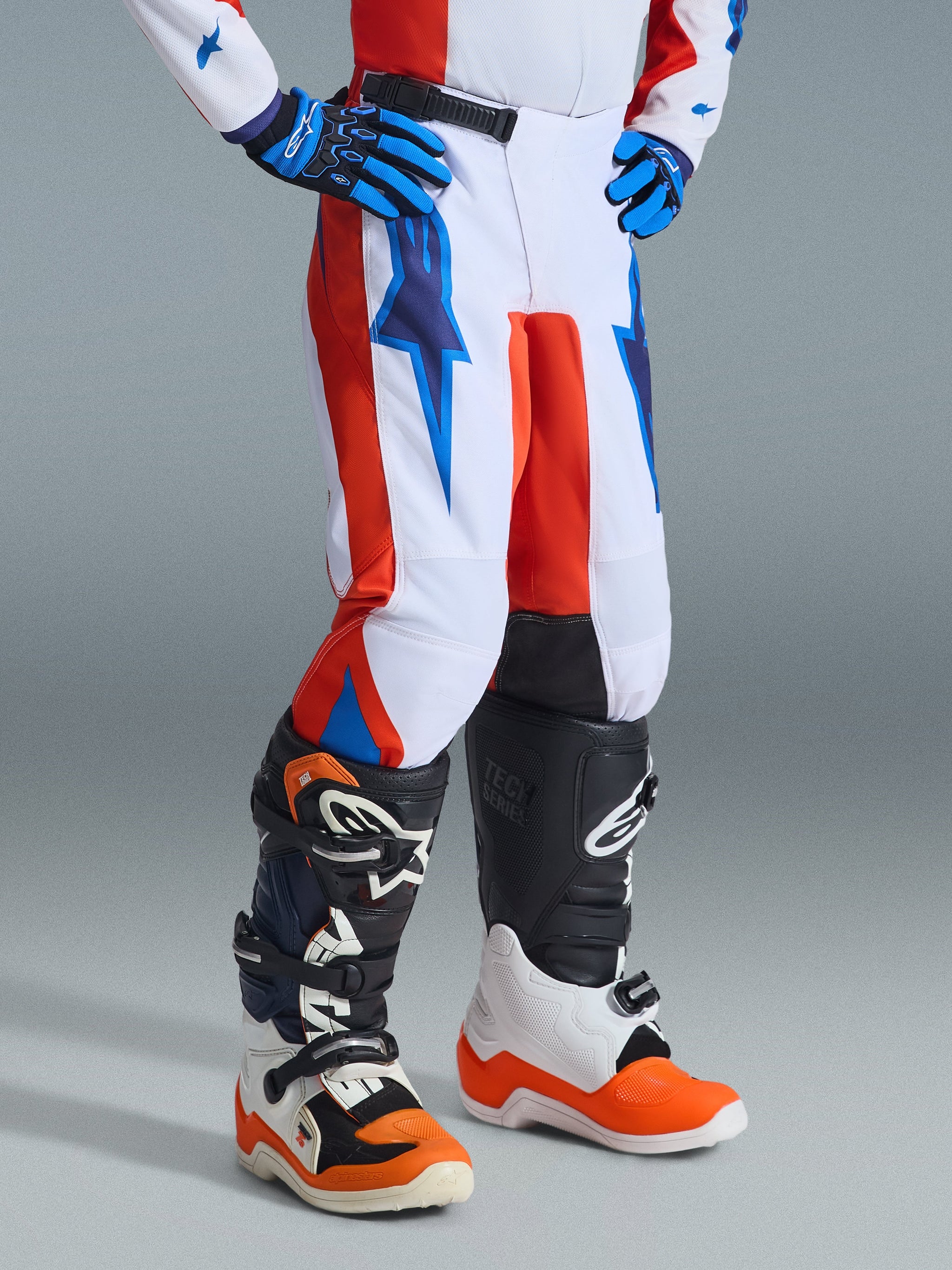 Alpinestars 2026 Youth Fluid Grid Pants, Motocross Pants, Orange and UCLA Blue on white, worn with matching gloves and off-road boots, featuring bold lightning-style graphics and durable construction for youth riders