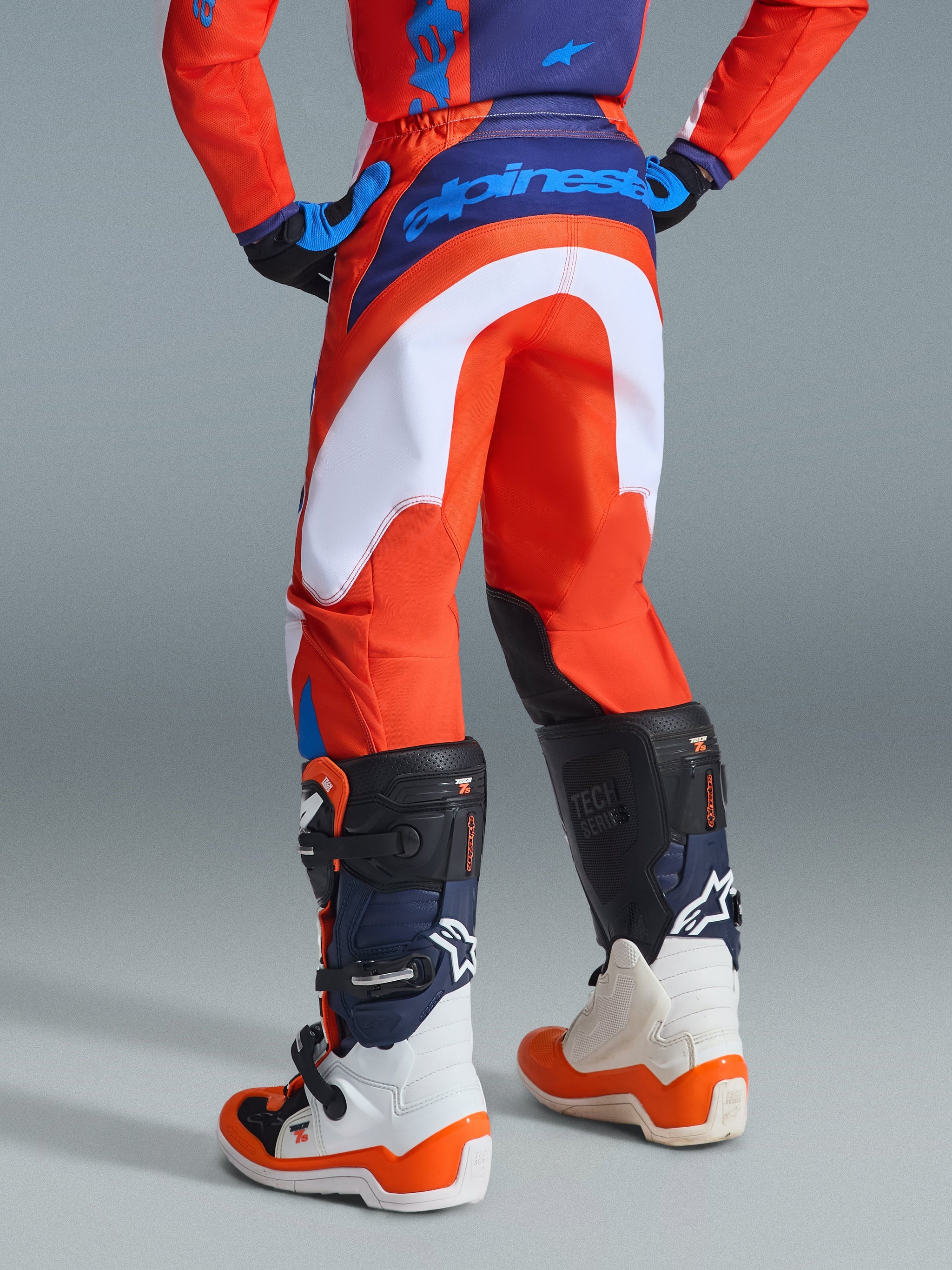Alpinestars 2026 Youth Fluid Grid Pants, Motocross Pants, Orange and UCLA Blue, rear view on a rider wearing matching jersey and white boots, featuring bold white panels and blue branding on the waist, durable material for off-road racing