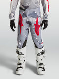 Alpinestars Fluid Jugend-Hose Lone 2027, Motocross-Hose, Grau und Rot mit Camo-Design, strapazierfähiges Polygewebe, getragen mit weißen Motorradstiefeln.