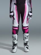 Alpinestars 2026 Stella Techstar Nomur Damen-Hose, Motocross-Hose, Schwarz, Weiß und Fuchsia, getragen mit passendem Renntrikot, Handschuhen und weißen Motocross-Stiefeln, mit auffälligen pinken Grafiken und Astars-Logos an den Knien, konzipiert für hochkarätigen Offroad-Wettbewerb.