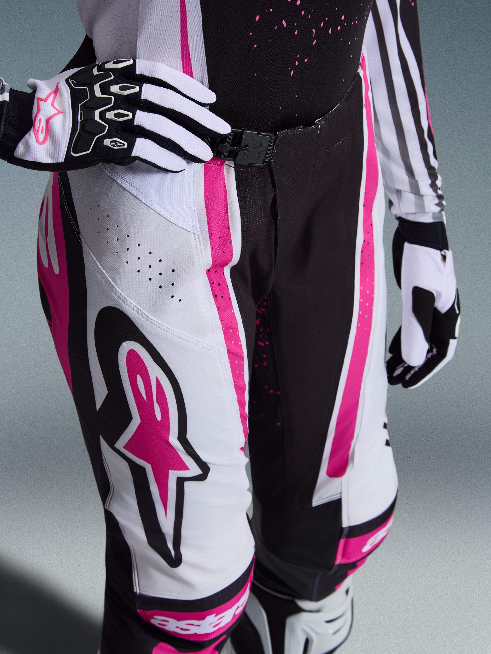 Alpinestars 2026 Woman Stella Techstar Nomur Pants, Motocross Pants, Black White and Fuchsia, featuring a large pink star logo on the thigh, laser-cut ventilation holes, and a secure waist buckle, worn with matching gloves and jersey.