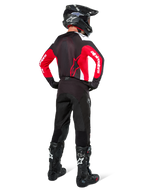 Motocross-Fahrer in der Rückansicht, Alpinestars Pro-Dura Jersey in Schwarz, Hellrot und Weiß, kombiniert mit schwarzer Motocross-Hose, Helm und Stiefeln, zeigt das Rückendesign und die Ärmellogos, abgestimmte Offroad-Rennausrüstung.