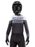 Motocross-Fahrer im Alpinestars Pro-Dura Jersey in Black Magnet White, langärmliges Performance-Oberteil mit weißen und grauen Farbblöcken, kombiniert mit schwarzem Helm und Schutzbrille, Alpinestars-Branding und „ONE GOAL ONE VISION“-Slogan, Offroad-Motorrad-Rennbekleidung