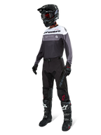 Alpinestars Pro-Dura Trikot in Black Magnet White, Motocross-Fahrer in voller Ausrüstung mit schwarzer Hose, schwarzem Helm mit Brille und schwarz-weißen Stiefeln, technisches Color-Block-Design mit weißen, grauen und schwarzen Paneelen, entwickelt für Enduro- und Offroad-Performance