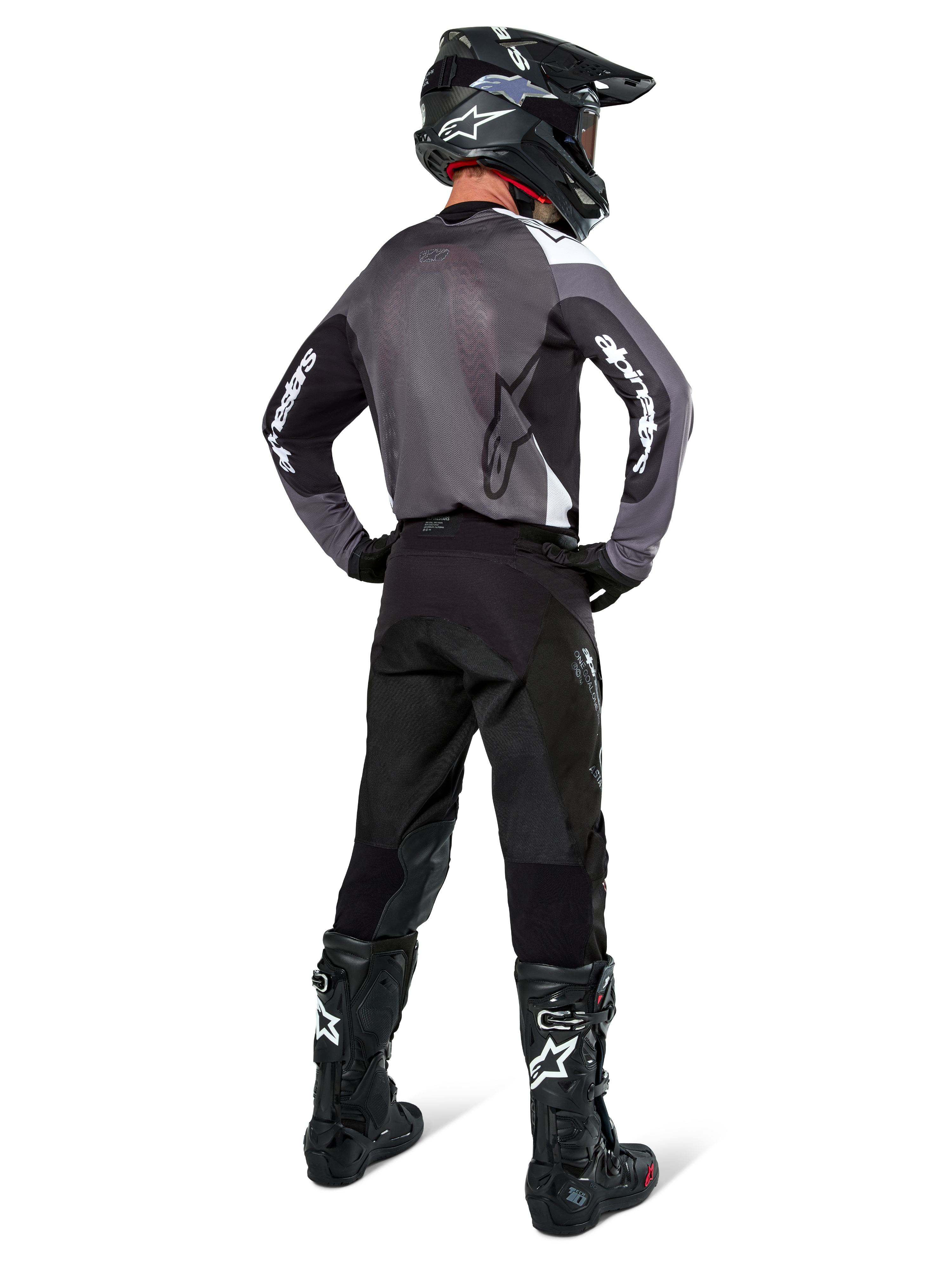Motocross-Fahrer im Alpinestars Pro-Dura Trikot in Black Magnet White, Rückansicht mit grauem Mesh-Rückenteil und schwarzen Ärmeln mit weißem Alpinestars-Branding, kombiniert mit schwarzer Hose, schwarzem Helm und schwarz-weißen Stiefeln, professionelle Enduro-Rennausrüstung