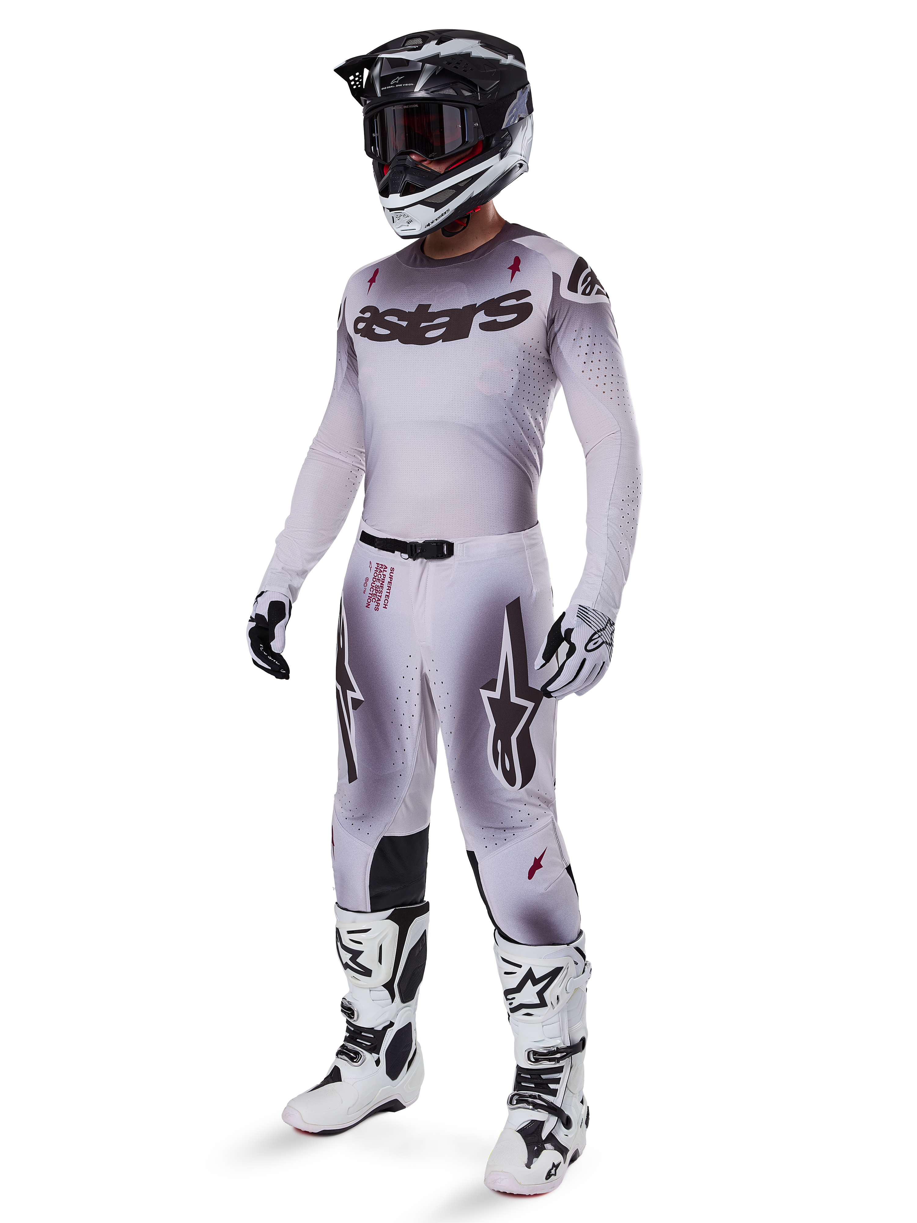 Motocross rider wearing complete racing gear, grey and white gradient jersey with black 'astars' branding, matching pants with red accents and star logos, black and white helmet with dark goggles, white Alpinestars Tech 10 Boots, professional off-road racing outfit