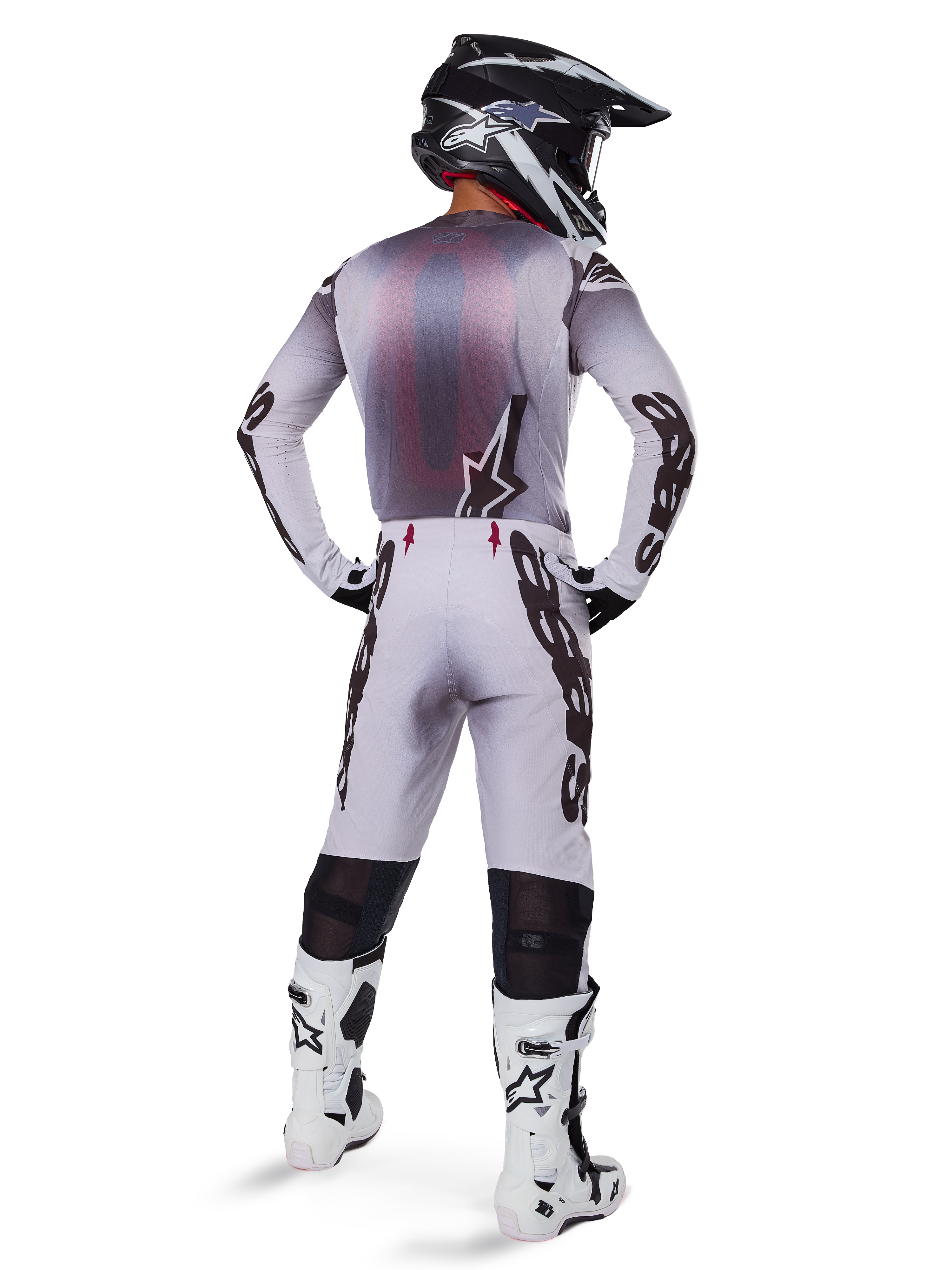 Motocross rider from behind wearing Alpinestars 2025 Supertech Maker Pants in Silver and Black, matching long-sleeve jersey, black and white helmet, and white and black boots, featuring bold black branding on the legs, professional off-road racing gear.