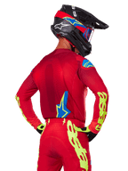 Rückansicht eines Motocross-Fahrers im Alpinestars 2025 Supertech Maker Gear Set in Rot, mit einem roten Trikot mit neongelbem Branding an den Ärmeln, einer passenden roten Hose, einem schwarzen Helm mit blauen und roten Akzenten sowie dazu passenden schwarz-gelben Handschuhen.