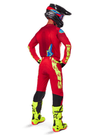 Motocross-Fahrer in der Rückansicht, trägt das Alpinestars 2025 Supertech Maker Trikot in Hellrot und Gelb Fluo, dazu passende Hose mit gelbem Branding, neongelbe Stiefel und einen schwarz-roten Helm, koordiniertes Outfit für den Profi-Offroad-Rennsport