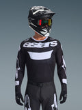 Alpinestars 2026 Racer Air Riway Jersey, schwarz-weißes Motocross-Trikot mit 'astars'-Branding, getragen von einem Fahrer mit passendem schwarzem Helm, Goggles und Hose, mit atmungsaktiven Mesh-Einsätzen für den Offroad-Rennsport.